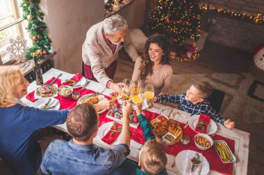 Masanın etrafında toplanmış güzel, mutlu bir ailenin yüksek açılı görüntüsü Noel yemeğini hep birlikte evde yiyor, Noel 'i kutluyor ve kadeh kaldırıyor.