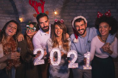 Yeni yıl partisinde eğlenen bir grup arkadaş, 2021 yılını gece yarısı geri sayımını temsil eden aydınlatıcı numaralar tutuyorlar.