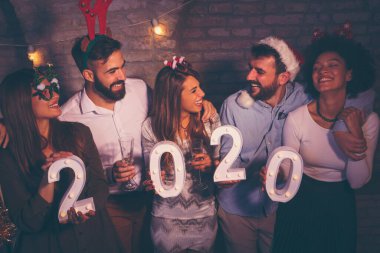 Yeni yıl partisinde eğlenen bir grup arkadaş, 2020 yılını gece yarısı geri sayımını temsil eden aydınlatıcı numaralar tutuyorlar.
