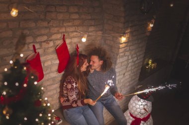 Güzel bir Noel ağacının yanında oturmuş, yeni yıl için gece yarısı gerisayımı için maytap sallayan güzel bir çift.