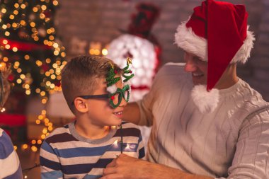 Baba ve oğul Noel ağacında eğleniyor, parti bardakları ve Noel Baba şapkası deniyor, kış tatilinin tadını çıkarıyor ve Noel arifesini evde birlikte kutluyorlar.