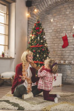 Mutlu anne ve kız Noel ağacının yanında oturuyor, Noel günü evde oynuyor ve eğleniyorlar.