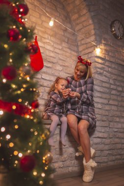 Güzel bir anne ve kızın güzel bir Noel ağacının yanında oturup oyun oynayarak, oje sürerek ve Noel arifesinde Noel Baba 'yı bekleyerek eğlendiği yüksek açılı bir manzara.