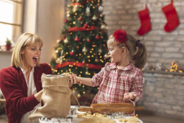 Anne ve kız Noel ağacının yanında oturmuş zencefilli çörekler için hamur yoğuruyor ve eğleniyorlar.