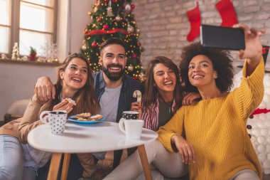 Bir grup arkadaş Noel 'i evde kutluyor, kahve içiyor, Noel kurabiyeleri yiyor ve akıllı telefon kullanarak selfie çekiyor.