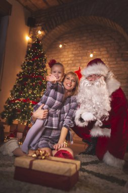 Anne ve kızı Noel arifesinde Noel ağacının yanında Noel Baba 'yla eğleniyorlar.