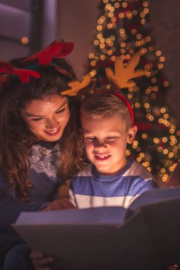 Güzel anne ve oğul Noel ağacının yanında oturmuş Noel arifesinde evde masal okuyorlar.