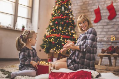 Mutlu anne ve kız Noel ağacının yanında oturuyor, Noel günü evde oynuyor ve eğleniyorlar.