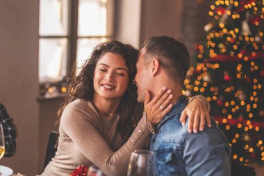 Güzel bir çift Noel yemeği yiyor, masada oturuyor, Noel hediyelerini alırken sarılıyor ve öpüşüyor.