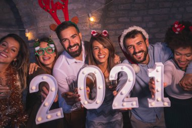 Yeni yıl partisinde eğlenen bir grup arkadaş, 2021 yılını gece yarısı geri sayımını temsil eden aydınlatıcı numaralar tutuyorlar.