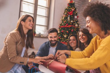 Bir grup arkadaş, kış tatillerini evde birlikte geçirip Noel hediyelerini paketlerken eğleniyorlar.