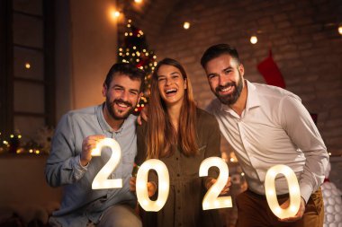 Yeni yıl partisinde eğlenen bir grup genç arkadaş, 2020 yılını temsil eden aydınlatıcı numaralar tutuyorlar. Geceyarısı geri sayımı temsil ediyorlar.