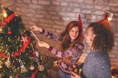 Güzel, genç bir çift Noel 'i evde kutlarken ve birlikte Noel ağacı süslerken eğleniyor.