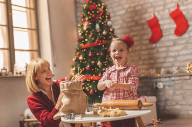 Anne ve kız Noel ağacının yanında oturmuş zencefilli kurabiye yapıyor ve eğleniyorlar.