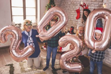 Güzel mutlu bir aile Noel 'i evde kutluyor, 2020 numaralı dev balonları tutarak eğleniyor, gelecek yeni yılı temsil ediyor.