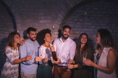 Bir grup arkadaş birlikte yeni yılı kutluyor, gece yarısı geri sayımında eğleniyor, şampanya şişesini açıyor ve kadeh kaldırıyor.