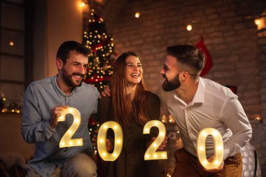 Yeni yıl partisinde eğlenen bir grup genç arkadaş, 2020 yılını temsil eden aydınlatıcı numaralar tutuyorlar. Geceyarısı geri sayımı temsil ediyorlar.