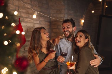 Bir grup genç arkadaş Noel 'i birlikte kutluyor, kadeh kaldırıyor ve şarap içiyor.