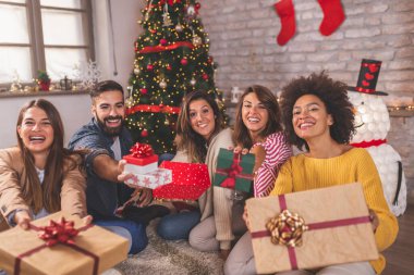 Bir grup arkadaş Noel 'i evde kutlarken eğleniyorlar, güzelce paketlenmiş Noel hediyelerini tutuyorlar.