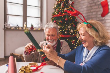 Kıdemli çift Noel 'i evde kutluyor, güzel süslenmiş Noel ağacının yanında oturuyor, Noel hediyelerini paketlerken eğleniyorlar.