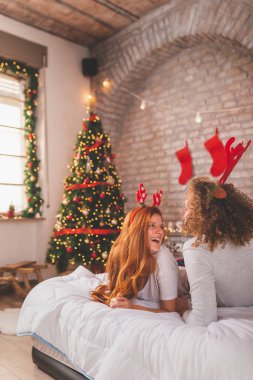 Birbirine aşık bir çift pijama ve geyik boynuzu kostümü giyiyor Noel sabahı yatakta uzanıyor, eğleniyor ve birlikte vakit geçiriyorlar.