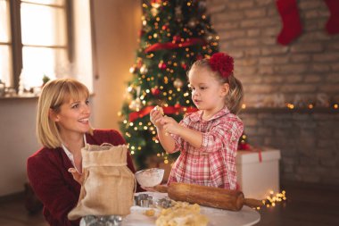 Anne ve kızı güzelce süslenmiş Noel ağacının yanında oturmuş zencefilli kurabiye pişiriyor ve eğleniyorlar.
