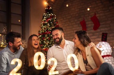 Yeni yıl partisinde eğlenen bir grup genç arkadaş, 2020 yılını temsil eden aydınlatıcı numaralar tutuyorlar. Geceyarısı geri sayımı temsil ediyorlar.