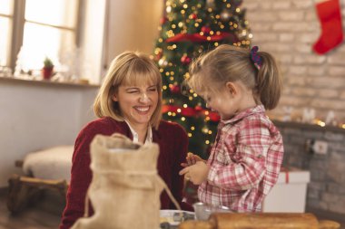 Anne ve kız Noel ağacının yanında oturmuş zencefilli kurabiye yapıyor ve eğleniyorlar.