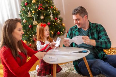 Ebeveynler küçük kızlarıyla oynuyorlar, kağıt kar taneleri kesiyorlar ve evde Noel süslemeleri yaparken eğleniyorlar.