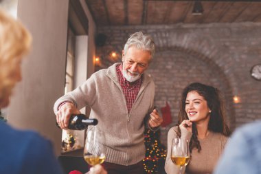 Genç ve güzel bir çift aileleriyle Noel yemeği yiyor. Masanın etrafında toplanmış genç bir kadının babası şarap dolduruyor.