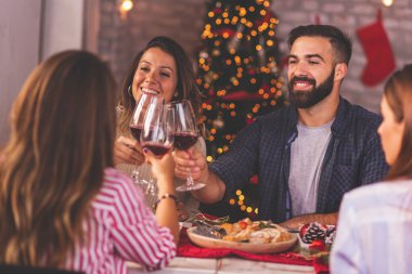 Arkadaşlar Noel yemeğinde masanın etrafında toplandılar, kadeh kaldırdılar, şarap kadehlerini kaldırdılar ve tatil sezonunu birlikte geçirerek eğlendiler.