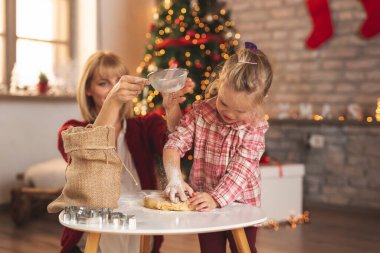 Anne ve kız Noel ağacının yanında oturmuş, zencefilli Noel kurabiyeleri yapıyor ve kış tatilinde evde vakit geçirirken eğleniyorlar.