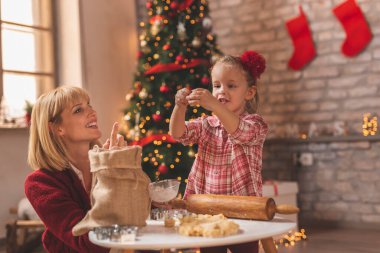 Anne ve kızı güzelce süslenmiş Noel ağacının yanında oturmuş hamuru saklarken eğleniyorlar ve zencefilli Noel kurabiyesi yapıyorlar.