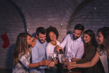 Bir grup arkadaş birlikte yeni yılı kutluyor, gece yarısı geri sayımında eğleniyor, şampanya şişesini açıyor ve kadeh kaldırıyor.