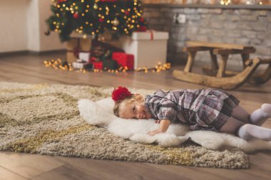 Çocuk güzel dekore edilmiş bir Noel ağacının yanında halıya uzanmış, Noel günü evde eğleniyor, gülümsüyor ve oynuyor.