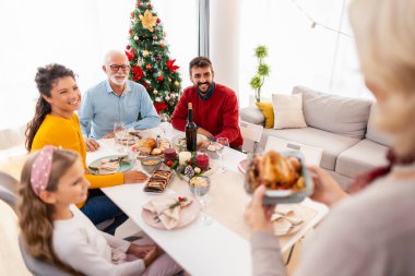 Güzel, mutlu bir aile masanın etrafında toplandı, Noel yemeğini hep birlikte evde yiyorlar, bir kadın masaya tavuk getiriyor ve yemek getiriyor.