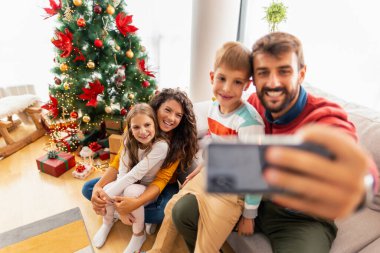 Aile Noel 'i evde kutluyor, Noel ağacının yanında selfie çekiyor.