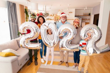 Güzel mutlu bir aile Noel 'i evde kutluyor, 2022 numaralı dev balonları tutarak eğleniyor, gelecek yeni yılı temsil ediyor.