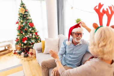 Son sınıf çifti kanepede oturup Noel Baba şapkası ve geyik boynuzlarını deniyorlar. Noel 'i evde birlikte kutluyorlar.