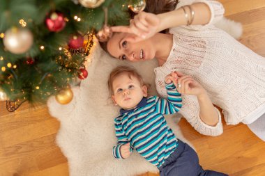 Güzel, genç bir annenin Noel sabahı oğluyla oynayıp, güzelce süslenmiş Noel ağacının altında yatışının en güzel görüntüsü.