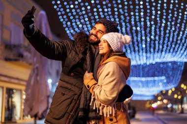 Güzel, genç ve aşık bir çift şehrin sokaklarında Noel arifesini kutlarken selfie çekerken eğleniyor.
