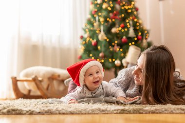 Anne, Noel 'i evde kutlarken bebeğiyle oynuyor. Süslü bir Noel ağacının yanında uzanıyor ve sarılıyor.