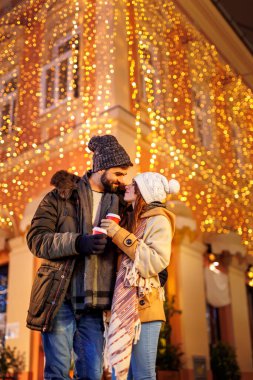 Güzel, genç ve aşık bir çift dekore edilmiş şehir sokaklarında yürürken dışarıda Noel 'i kutlarken sıcak sıcak sıcak şarap içerken eğleniyor.