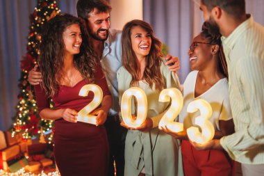 Yeni yıl partisinde eğlenen bir grup genç arkadaş, 2023 yılını temsil eden aydınlatıcı numaralar taşıyor.
