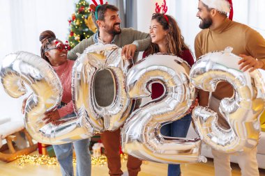 Bir grup genç arkadaş, 2023 numaralı dev balonları tutarak evde yeni yılı kutluyor.