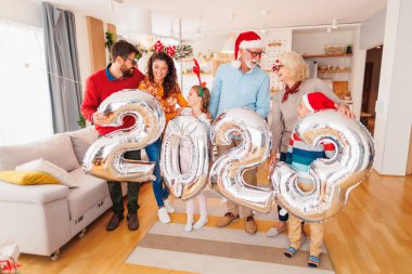 Güzel mutlu bir aile Noel 'i evde kutluyor, 2023 numaralı dev balonları tutarak eğleniyor, gelecek yeni yılı temsil ediyor.