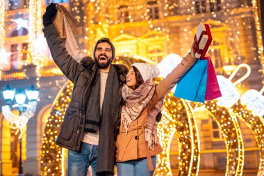 Mutlu çift Kara Cuma için alışveriş yaparken eğleniyor, süslü şehir sokaklarında alışveriş torbalarıyla yürüyor.