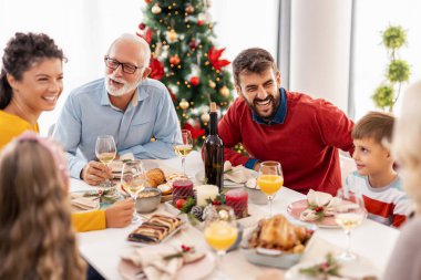 Güzel, mutlu bir aile masanın etrafında toplanmış, birbiriyle konuşuyor ve evde hep birlikte Noel yemeği yerken gülüyorlar.