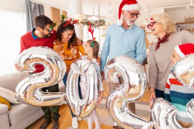 Güzel mutlu bir aile Noel 'i evde kutluyor, 2023 numaralı dev balonları tutarak eğleniyor, gelecek yeni yılı temsil ediyor.