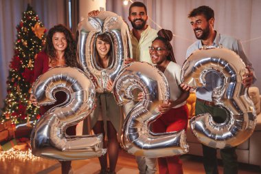 Yeni yılı temsil eden 2023 numaralı balonları tutan neşeli bir grup genç arkadaş.